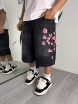 Bermuda baggy de denim negro con efecto lavado, corte holgado por debajo de las rodillas y delicado bordado floral de ramas con flores rosadas en el lateral.
