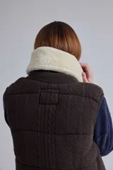Chaleco tejido de punto color marrón con cuello de piel sintética, cierre frontal con cursor de cuero y diseño acolchado con cortes horizontales.