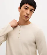 Remera de manga larga estilo Henley, confeccionada en tejido texturizado color beige, con cuello redondo y cierre frontal parcial de botones.
