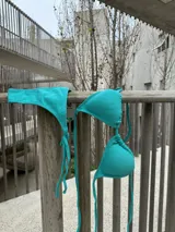 Bikini de dos piezas color turquesa, con top de triángulos movibles para atar al cuello y espalda, y almohadillas desmontables. La bombacha es colaless, también de atar.