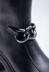 Botas negras de símil cuero, caña corta, punta redonda, plataforma tipo tractor de 6cm de alto y aplique de cadena plateada en el frente.
