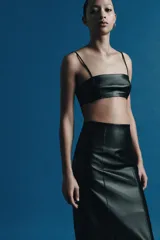 Falda midi de tiro medio, color negro, confeccionada en piel 100% con pespuntes marcados a tono y bajo recto. Cierre lateral con cremallera oculta en costura.