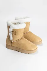 Bota tipo pantubota color beige, confeccionada en material gamuzado con interior y borde superior de piel sintética blanca. Presenta un detalle de botón lateral y suela de goma antideslizante.