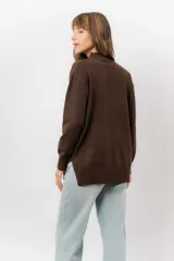 Sweater de tejido de punto color marrón, con cuello alto, corte relajado y terminaciones en rib en puños y cintura. Presenta una hilera de botones metálicos decorativos en uno de los laterales.