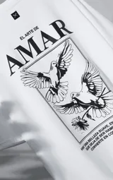 Remera blanca de corte oversize con cuello redondo y manga corta. Presenta una estampa gráfica en la espalda con diseño de palomas, flores y texto en español.