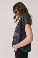Remera gris oscuro de corte holgado, con cuello redondo y mangas cortas. Presenta un estampado frontal alusivo a Tom Petty and the Heartbreakers con motivos de corazón, guitarra y texto estilo vintage.