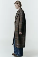 Abrigo largo de corte oversize con estampado de cuadros en tonos marrones y líneas azules. Presenta cuello de solapa, cierre frontal cruzado con botones, mangas largas y bolsillos delanteros con solapa.