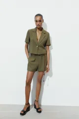 Bermuda de tiro alto en color verde militar, con cintura elástica y detalle de cinturón fino trenzado con abalorios decorativos.