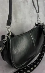 Cartera tipo baguette de cuero sintético negro con acabado brillante, cierre superior y correa ancha decorada con tachas metálicas plateadas.