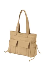 Cartera tipo shopper de poliuretano color beige, con dos bolsillos frontales con solapa, tirantes largos para el hombro y cordones ajustables en los laterales.