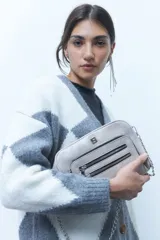 Bandolera pequeña de cuero vegano color gris claro, con dos cierres horizontales en el bolsillo frontal y un logo metálico cuadrado. Incluye correa de cadena y correa ajustable de cuero vegano.