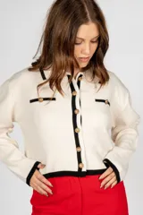 Saco corto de punto color negro con cuello polo, cierre frontal con botones dorados y ribete blanco en cuello, puños y ruedo.