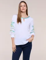 Blusa blanca de silueta semi entallada, confeccionada en tejido texturado. Cuenta con escote en V con abertura y vivo bordado multicolor, mangas 3/4 abullonadas con bordados, calados y puños elásticos.