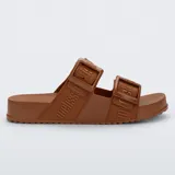 Sandalias Melissa Cozy Slide M-Lover color marrón, con diseño de dos tiras anchas con hebillas ajustables y tiras de tela con la marca estampada. Confeccionadas en PVC extra flexible, con plantilla anatómica y suela dentada.