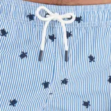 Short de baño con diseño de rayas verticales blancas y celestes, decorado con pequeños estampados de tortugas en color azul marino. Cuenta con cintura elástica y cordón ajustable blanco.