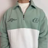 Buzo de algodón con medio cierre frontal y cuello tipo polo. Presenta un diseño de bloques de color en tonos gris oscuro y blanco, con bordados decorativos en el pecho.
