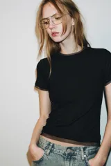 Camiseta de manga corta color marrón oscuro con textura acanalada, cuello redondo y bajo recto. Presenta un bajo superpuesto de tul o tela más clara, visible en el ruedo y en el cuello.