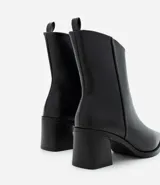 Bota corta de cuero sintético negro con diseño asimétrico en la caña, punta fina, taco bloque mediano y tirador trasero.