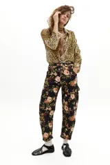 Pantalón de denim con corte barrel y tiro medio, estampado con diseño floral de rosas sobre fondo negro. Cuenta con pretina con pasacintos, bolsillos frontales, laterales y traseros, y largo hasta el tobillo.
