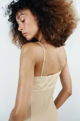 Vestido midi de color beige con escote recto adornado con un panel de encaje semitransparente, tirantes finos ajustables y falda fluida con cierre lateral con cremallera oculta.