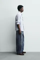 Camisa de corte regular fit confeccionada en tejido de algodón con diseño de rayas verticales. Presenta cuello abotonado, manga larga con puños abotonados, bolsillo plastrón en el pecho y cierre frontal con botones.