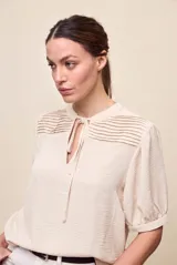 Blusa de manga corta color negro, con calce relajado, escote redondo con abertura y lazo para anudar. Presenta detalles de tablas horizontales en la parte superior que aportan textura al diseño.