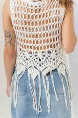 Top tejido artesanal color crudo, confeccionado en punto calado con diseño protagonista. De silueta recta y calce relajado, presenta escote amplio y terminación inferior con flecos.