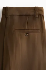 Pantalón sastrero de corte ancho, color marrón, con pinzas frontales, trabillas para cinturón y raya marcada en las piernas.