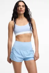 Top deportivo de microfibra en color beige con detalles de ribetes y banda inferior en color marrón. Presenta diseño de espalda estilo nadadora y logo de la marca estampado en la banda elástica inferior.