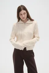 Saco de punto de algodón con diseño de trenzas, cuello alto y cierre frontal completo. Presenta un corte al cuerpo y mangas largas.