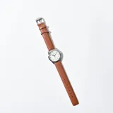 Reloj de pulsera con correa marrón símil cuero y esfera blanca con números arábigos.