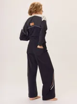 Pantalón de corte ancho y estilo comfy, confeccionado en algodón color marrón. Presenta detalles de franjas verticales en tonos beige y rojo a lo largo de las piernas, con cintura elástica.