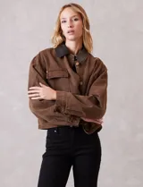 Campera de denim color marrón, con cuello de solapa en ecocuero negro. Cierre frontal con botones y bolsillos delanteros. Forro interno a tono.