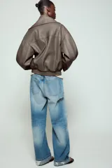 Cazadora Zara Woman Collection de efecto piel con cuello solapa ancho, manga larga, bolsillos delanteros y bajo elástico. Presenta un cierre frontal cruzado con botón a presión.