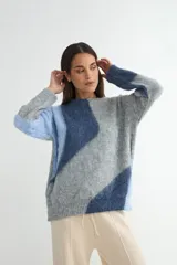 Buzo de tejido de punto con diseño de bloques de color en tonos blanco y gris, de cuello redondo y manga larga.