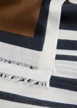 Pañuelo fluido de tejido ligero, con diseño estampado que combina secciones en blanco con lunares negros, un panel en negro con lunares blancos, y una franja inferior en marrón y gris con detalles de rayas. Presenta terminaciones deshilachadas en los bordes.