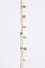Collar doble dorado con una tira de perlas intercaladas con pequeñas piedras de colores y otra cadena metálica con dijes colgantes de piedras rectangulares y perlas. Cuenta con cierre de mosquetón y cadena de alargue.