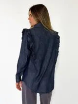 Camisa de denim azul oscuro con cuello clásico, cierre frontal de botones y detalle de volados en los hombros.