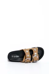 Sandalia plana color beige con dos tiras anchas decoradas con hebillas grandes y apliques metálicos plateados de estilo western, sobre suela negra.