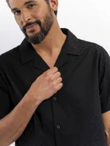 Camisa de manga corta color negro con sutil patrón tipo damero, cuello cubano y cierre frontal con botones.