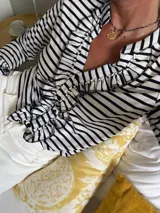 Blusa de manga larga a rayas verticales blancas y negras con volados en el frente y en el escote.