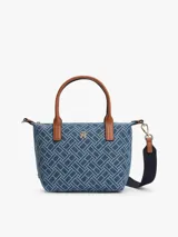 Cartera tote compacta Tommy Hilfiger de tejido denim con estampado geométrico integral del monograma TH, asas superiores en tono marrón y correa de hombro ajustable y extraíble. Cuenta con cierre de cremallera y herrajes dorados.