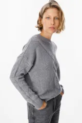 Sweater de punto gris con cuello redondo, diseño holgado y detalle de tejido en espiga en el frente y las mangas. Presenta puños y ruedo acanalados.