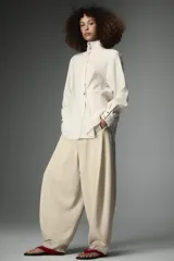 Pantalón de tiro medio con diseño tipo balloon, confeccionado en lyocell. Presenta pierna ancha, bolsillos delanteros ocultos en costura y cierre frontal con cremallera, botón y ganchos metálicos.