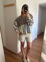 Sweater de tejido de punto con silueta oversize, cuello redondo y mangas largas abullonadas. Presenta un diseño patchwork con rayas verticales en tonos rojo, rosa y gris verdoso en el cuerpo, y un estampado floral en tonos rosa y rojo con detalles dorados en las mangas. Los puños y el cuello tienen un ribete a rayas horizontales.