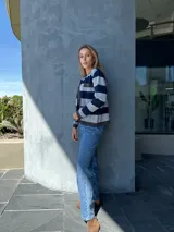 Chaqueta tejida en lana a rayas horizontales grises y azul marino, con cuello redondo, cierre frontal con botones dorados, bolsillos frontales con solapa y ribete en gris oscuro.