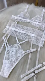 Conjunto de lencería de cuatro piezas en color blanco, confeccionado en encaje con diseño floral. Incluye bralette triangular, tanga de tiro alto con tiras ajustables, portaligas integrado y ligas para las piernas.