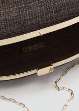 Bolso tipo clutch de diseño semiesférico en color marrón, confeccionado en rafia tejida, con cierre metálico superior a presión dorado y asa de cadena extraíble.