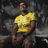 Camiseta de fútbol Puma del Club Peñarol, modelo Away Jersey. Diseño amarillo con detalles en negro en el cuello en V, los bordes de las mangas y líneas horizontales en el pecho. Incluye el logo de Puma, el escudo del club y el sponsor Antel.