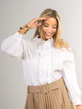 Camisa blanca con cuello alto con volados, cierre frontal con botones ocultos y mangas largas abullonadas.